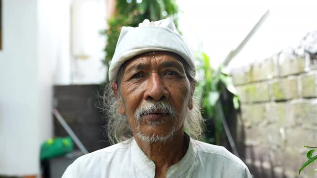 Portrait elderly man with a serene expression wearing a traditional white outfit and head covering, standing outdoors. Old man look at camera. His wrinkled face reflects wisdom and experience. 