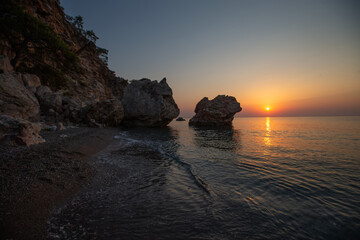 Seascape of rocky shore and setting sun.