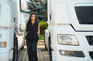 Portrait of female trucker proudly standing between trailers and truck vehicle. Transportation...