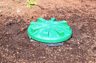 Covered sewer manhole of rural septic tank with green plastic cover, sewage system. Sewerage networks for country houses