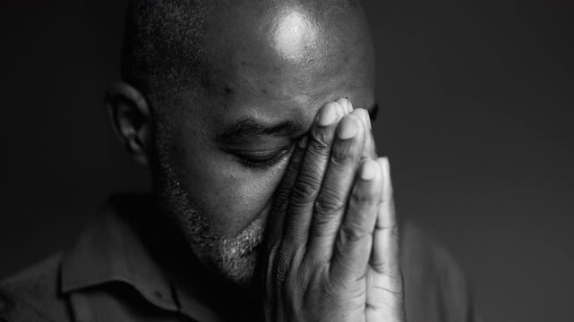 One Serious elderly black man in deep PRAYER asking for divine intervention during difficult times, close-up face of South American senior person of African descent in quiet contemplation monochrome