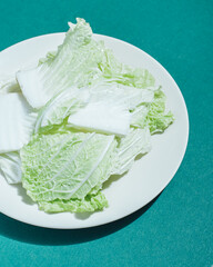 pieces of fresh iceberg lettuce on a white plate on a green background with hard shadow