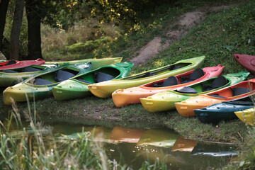 Many canoes of different colors on the river bank before training without people. Boating on the...