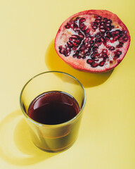 glass glass with pomegranate juice on a yellow background, half a pomegranate lies next to it