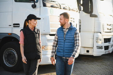 Two professional truck drivers stand in front of the big truck. They talk and perform a technical...