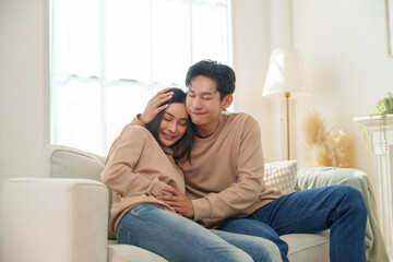 Obraz premium Asian couple sits comfortably on a sofa, the woman resting her head on the man shoulder, affectionate moment while relaxing at home.