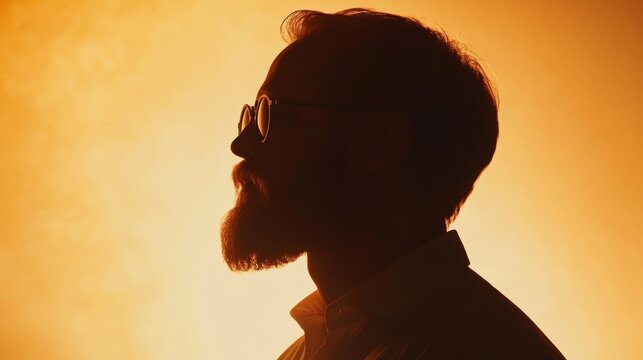 Silhouette of a bearded man wearing sunglasses, standing against a vibrant orange sunset backdrop, projecting a calm and thoughtful demeanor.