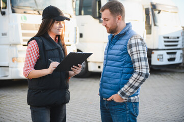 Logistics - proud driver or forwarder and female coworker, in front of trucks and trailers, on a...