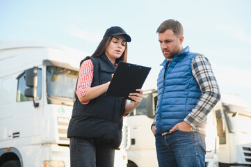 Logistics - proud driver or forwarder and female coworker, in front of trucks and trailers, on a...