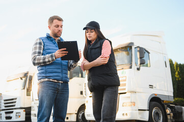 Two professional truck drivers stand in front of the big truck. They talk and perform a technical inspection of the vehicle before next drive. Professional transportation concept