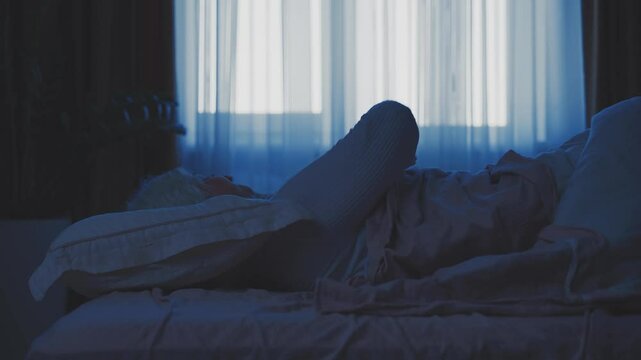 Senior woman suffers from insomnia lying down and can't sleep, tosses and turns in bed dark night room. blue moon light from window. lady old age restless sleep in soft pillow cozy bedroom rest relax