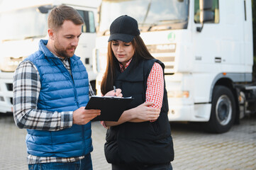 Two professional truck drivers stand in front of the big truck. They talk and perform a technical...