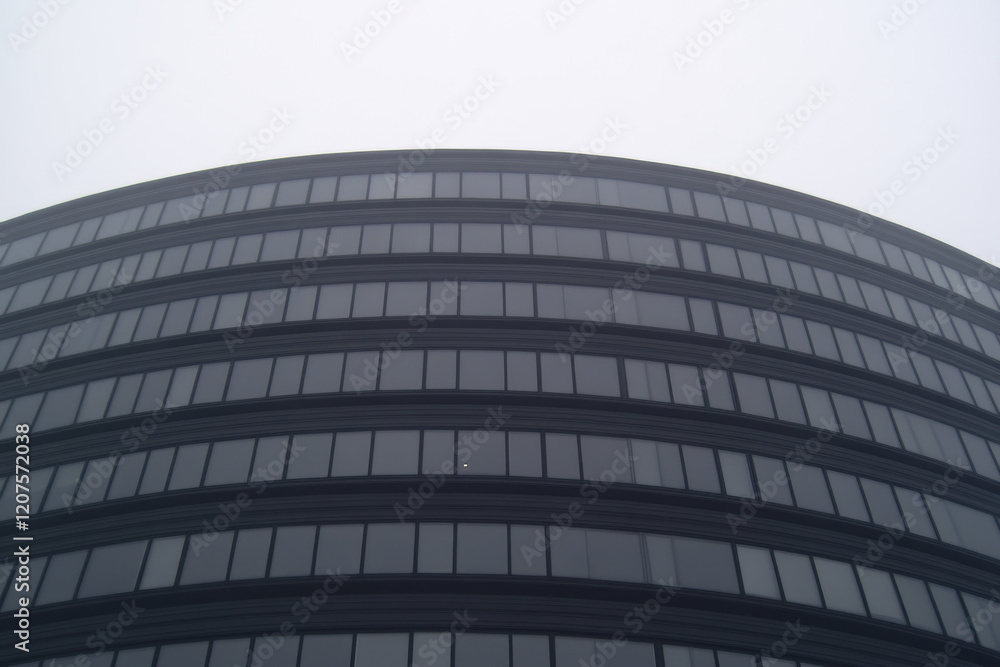 Poster a tall building with many windows and a gray sky in the background