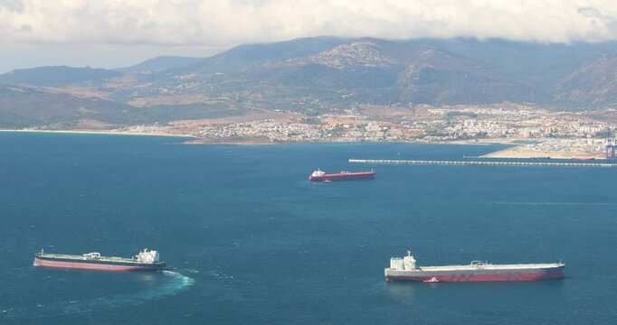 View from Gibraltar, British Overseas Territory and city on the Iberian Peninsula. Three large tankers at sea near a coastal city and mountains.