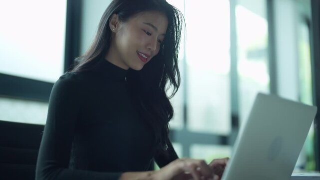 Asian businesswoman sits on chair using laptop typing keyboard at office/workplace