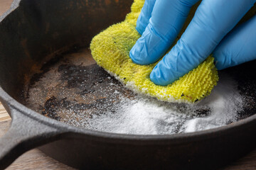 Person cleaning a rusty old cast iron fying pan using bicarbonate of soda and a scouring pad. On a...