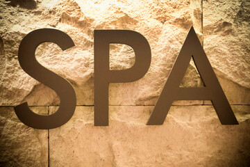 Serene Spa Retreat: Elegant Metallic Letters Spelling 'SPA' Set Against a Warm Yellow Stone...