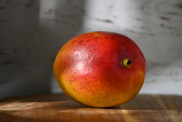 Vibrant mango resting on a wooden surface with soft light casting gentle shadows