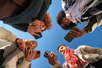 Obraz premium Four students are using their smartphones forming a circle, low angle view