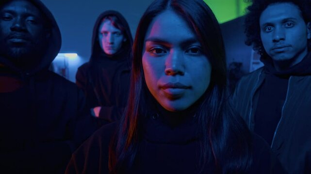 Zoom in group portrait of four confident multi-ethnic young hackers in black clothes posing for camera at nighttime