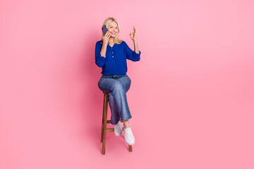 Full size photo of pretty senior female sit chair talk phone okey wear trendy blue outfit isolated on pink color background