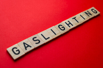 Word Gaslighting, written with wooden alphabet blocks, on red surface.