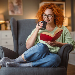 Obraz premium beauty redhead woman sit in the armchair and enjoy at coffee and book