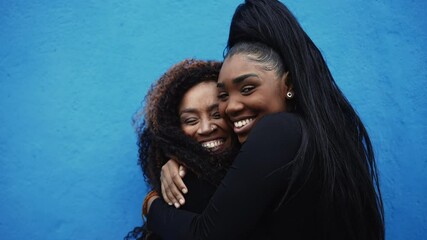 African American Adolescent daughter hugs mother in genuine affectionate love. Caring moment between parent and offspring on blue urban wall. Love and affection