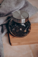 Close-up of a tea bag, loose tea, and a metal spoon on a wooden cutting board. A jar of tea stands...