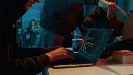 Tilt down view of young male fraudster engaging in illegal activities using laptop while two hackers working together in background