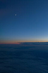 Sunset over the clouds. View from airplane window to the moon.