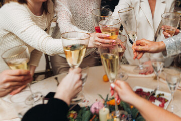 Group of guests celebrate and raise glasses, toasting and cheering with alcohol glasses with wine and champagne in the restaurant on corporate christmas birthday party event or wedding celebration
