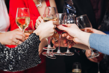 Group of guests celebrate and raise glasses, toasting and cheering with alcohol glasses with wine and champagne in the restaurant on corporate christmas birthday party event or wedding celebration