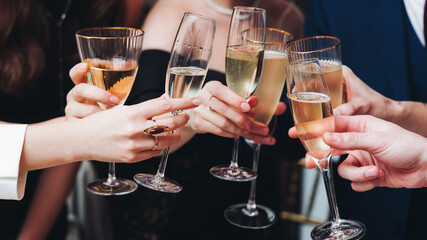 Group of guests celebrate and raise glasses, toasting and cheering with alcohol glasses with wine and champagne in the restaurant on corporate christmas birthday party event or wedding celebration