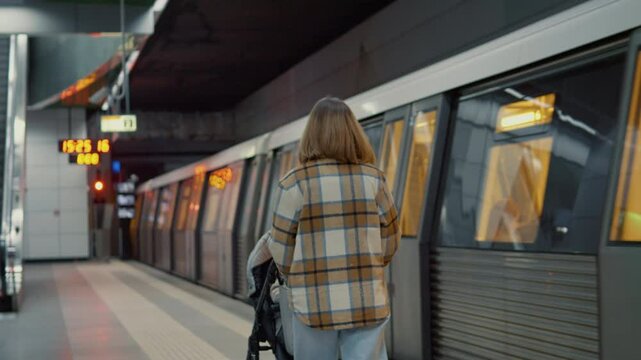 Young mother standing near subway platform, waiting with stroller while watching digital clock during daily commute in metropolitan station