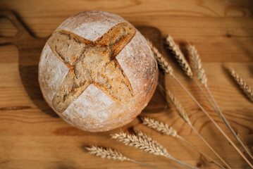loaf of fresh bread and spikelets on a wooden table
