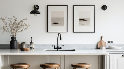 Elegant minimalist kitchen featuring framed black and white artwork, sleek sink, wooden bar stools, and stylish decor in neutral tones.