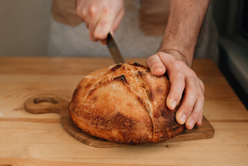 man slices fresh bread on a wooden table