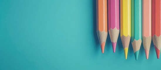 Vibrant multicolored pencils in a row on a bright turquoise background with ample negative space for creative text or design elements