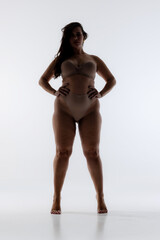 Photo of woman's silhouette, standing confidently in lingerie, holds hands on hips, show empowerment and boldness against white studio background. Concept of natural beauty, self love, confidence.