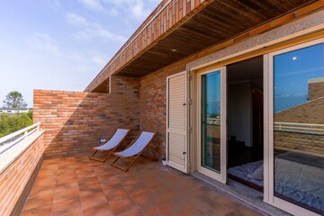 Brick terrace outdoors with two chairs and a large glass doors