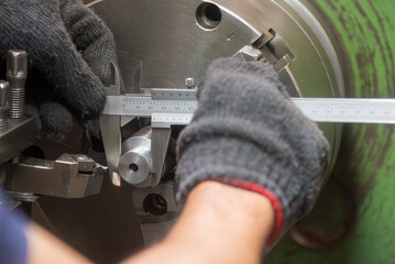 Close up scene the lath machine operator measuring dimension of turning parts by Vernier caliper.