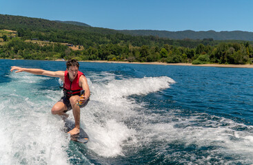 A cheerful young wake surfer in swimwear and a life vest filming himself with an action camera...