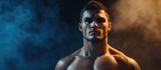 Muscular male athlete portrait in gym surrounded by blue and orange smoke with dramatic lighting and space for motivational text or fitness branding
