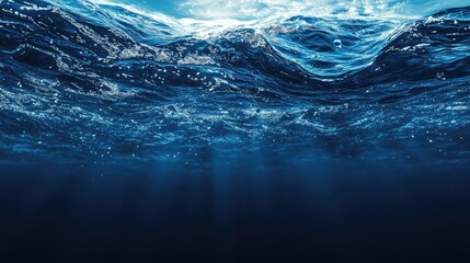 Fototapeta premium Underwater view of ocean waves with sunlight filtering through the surface, deep blue water background with Copy Space for text.