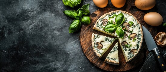 Cheese wheel with mushrooms and basil on wooden cutting board with eggs and knife on dark background Copy Space