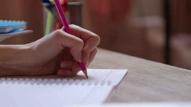 Close-up image of a woman's hand making notes in a notebook with a pencil. Businesswoman is compiling information on a sheet. Office table, brunette girl is writing important notes with her left hand