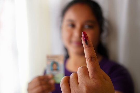 selective focus on ink-marked finger of an Indian village woman with smiling face and voter card on other hand.