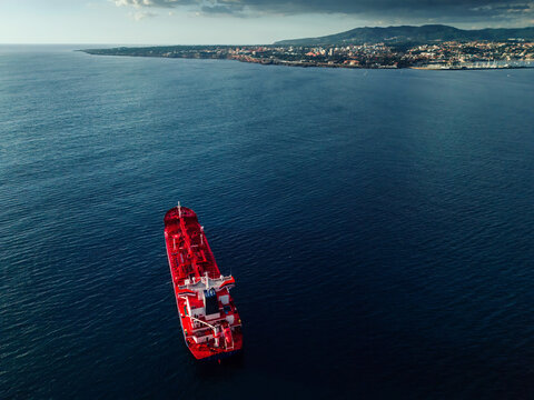 A large red cargo ship in calm waters, close to the shoreline of a coastal city, Portugal