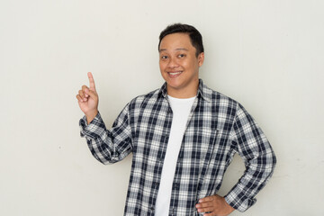 Fototapeta premium Attractive young Asian man smiling and pointing his finger to the side. Copy space. 